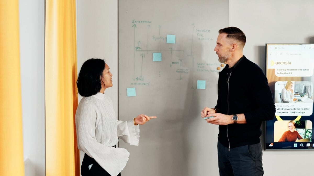 A female and a male colleague standing by a whiteboard discussing