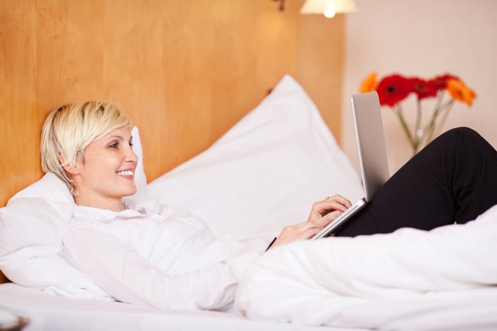 Young happy businesswoman using laptop while lying on bed in hotel room
